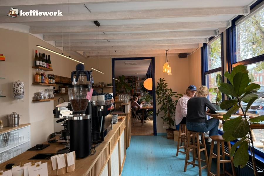 Inside a bright specialty coffee cafe in The Hague, with an espresso bar on one side and guests sitting near the front window.
